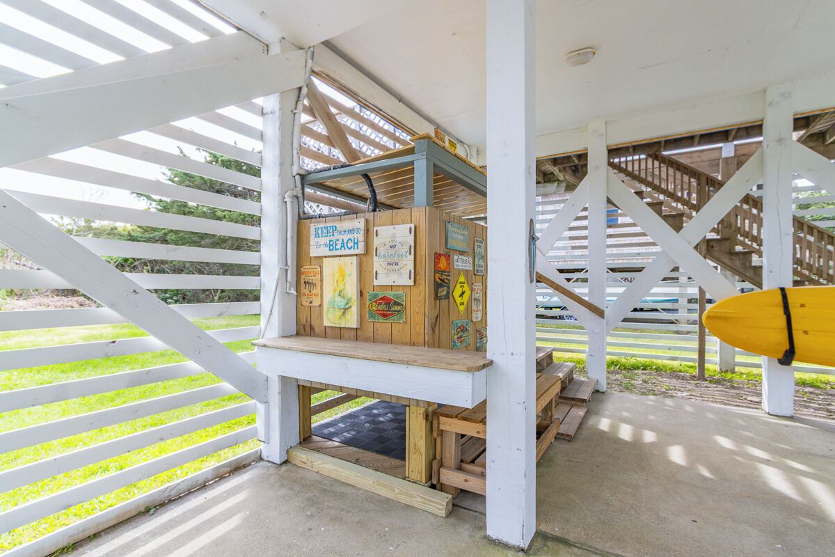 A covered outdoor area with a wooden bench, a surfboard, and various signs on the walls.