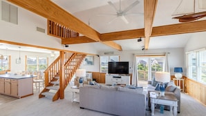 A spacious living area with a wooden staircase, a large TV, and a view of the outdoors. - Oceanside home in Hatteras 200 yards from beach, Hot Tub (Hatteras)