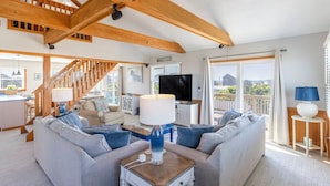 A spacious living room with a wooden staircase, a television, and a balcony with a view. - Oceanside home in Hatteras 200 yards from beach, Hot Tub (Hatteras)