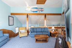 A living room with a blue sofa, a wooden coffee table, a yellow armchair, and a ceiling fan.