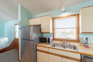 Cocina compacta con refrigerador, microondas, lavamanos y armarios de madera.