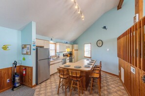 Une cuisine avec un îlot central, des chaises en bois, un réfrigérateur et une horloge au mur.