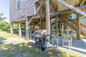 A wooden structure with a grill and chairs outside, suggesting a barbecue area.
