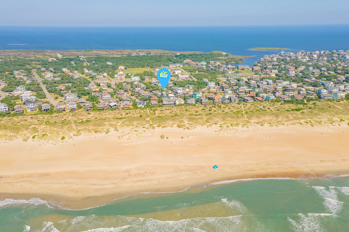 Vue aérienne d’une zone résidentielle côtière, avec des maisons, une plage et une étendue d’eau.