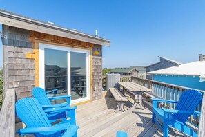 A wooden deck with blue chairs and a picnic table, overlooking a pool.