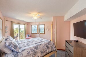 A bedroom with a bed, a ceiling fan, a television, and a window with a view.