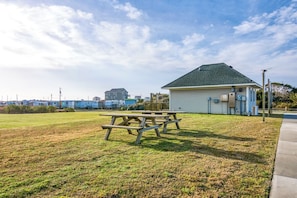 A picnic area with a wooden table and benches, a small building with a green roof, and a clear sky.