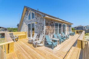 A wooden deck with Adirondack chairs and a small building with large windows.