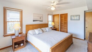 Un dormitorio con cama, ventilador de techo, mesita de noche con lámpara, armario de madera y una puerta.