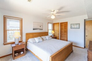 A bedroom with a bed, a ceiling fan, a nightstand with a lamp, a wooden wardrobe, and a door.