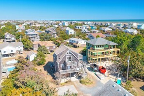 An aerial view of a residential area with houses, a large wooden structure, and a clear view of the ocean. - Oceanside home in Salvo w/ game room & hot tub (Salvo)