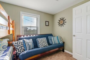 Una habitación con un sofá azul, una cama de madera, una ventana con persianas, una puerta y un reloj de pared.