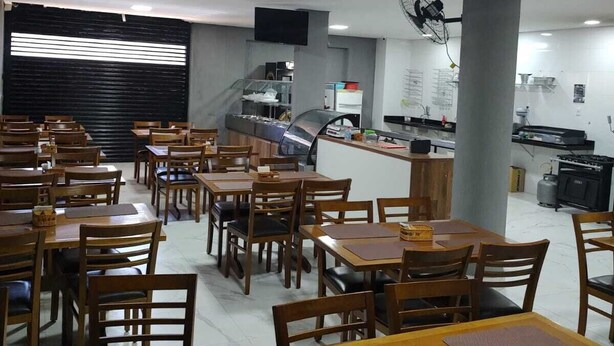 A restaurant with wooden tables and chairs, a kitchen area, and a large pillar. - Hotel londres (Gama)