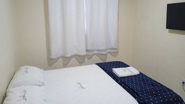 A single bed with a white mattress and a blue polka dot bedspread. There is a white curtain on the window, and an air conditioning unit is mounted on the wall. - Hotel londres (Gama)