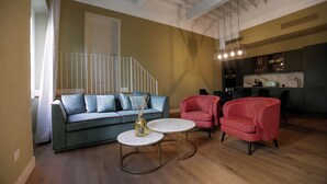 Ein Wohnzimmer mit einer Couch, zwei Sesseln, einem Couchtisch und einer Treppe, die zu einer oberen Etage führt.