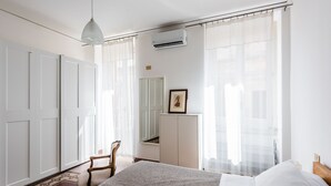 A bedroom with a bed, a chair, a wardrobe, and a picture frame on a cabinet.