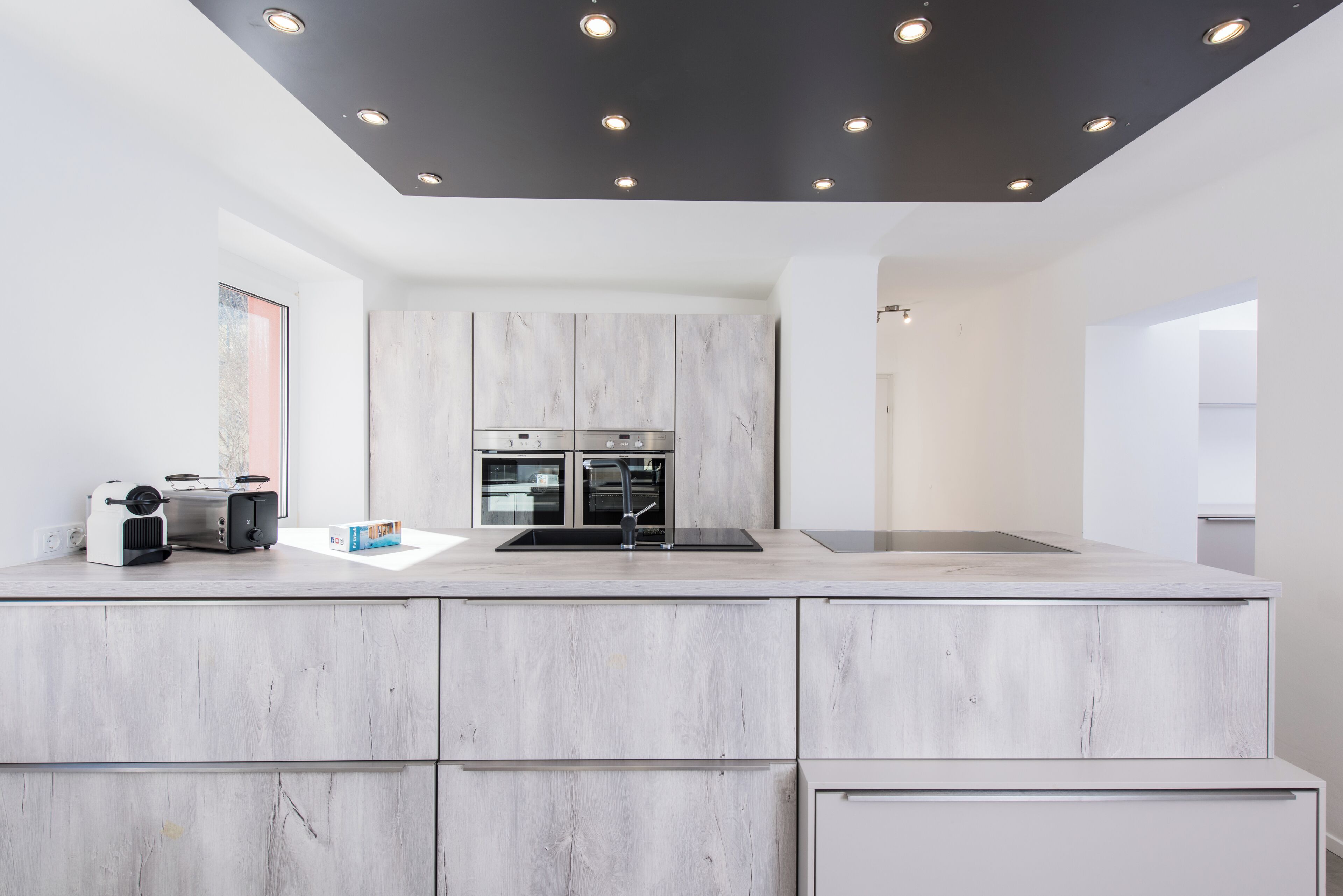 A modern kitchen with a marble countertop, built-in appliances, and recessed ceiling lighting.