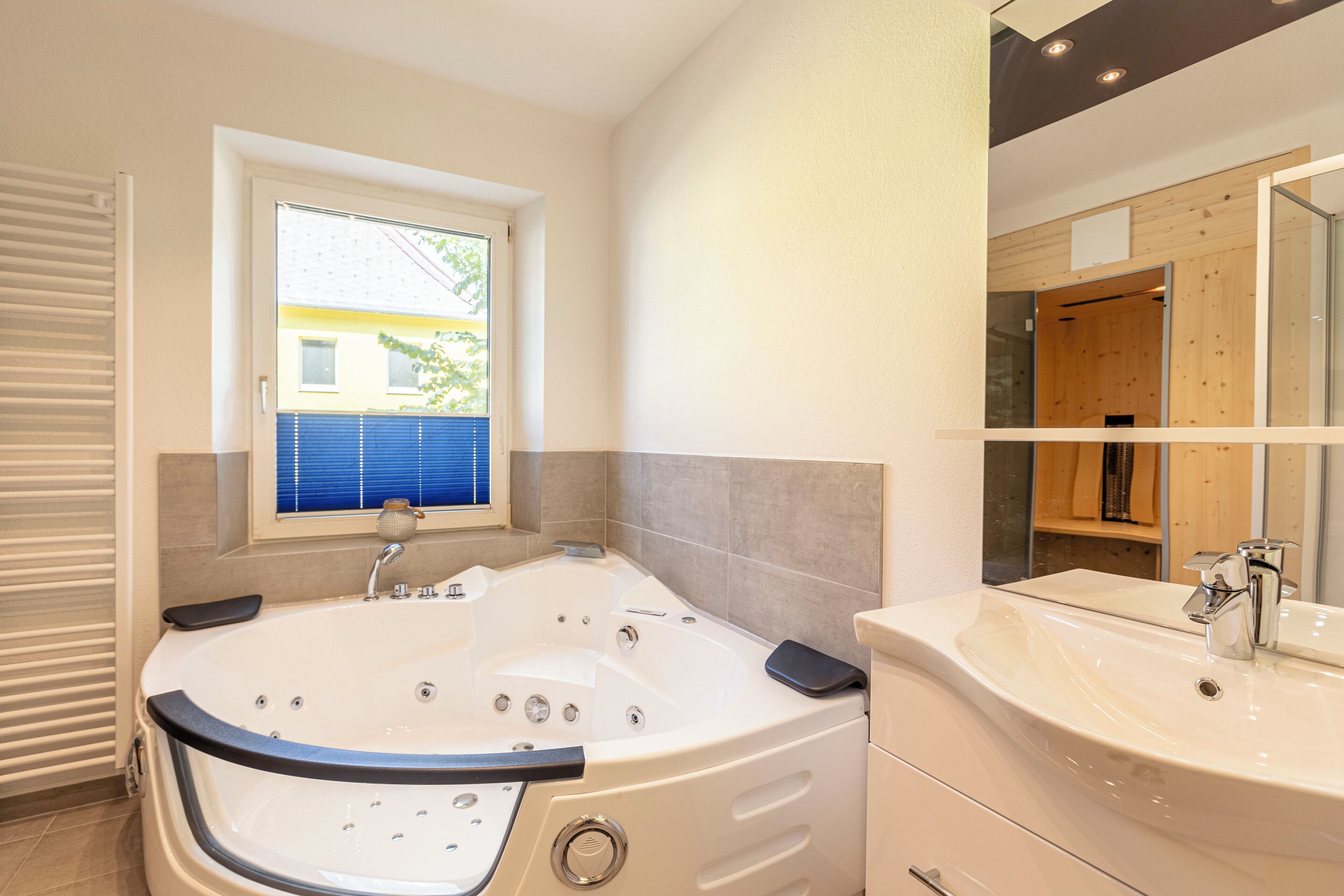 Ein modernes Badezimmer mit einer großen Badewanne, einem Waschbecken und einem Fenster mit Jalousien.