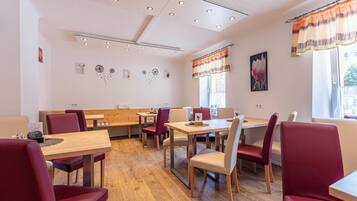 A dining area with wooden tables and chairs, a ceiling with recessed lighting, and wall decorations.