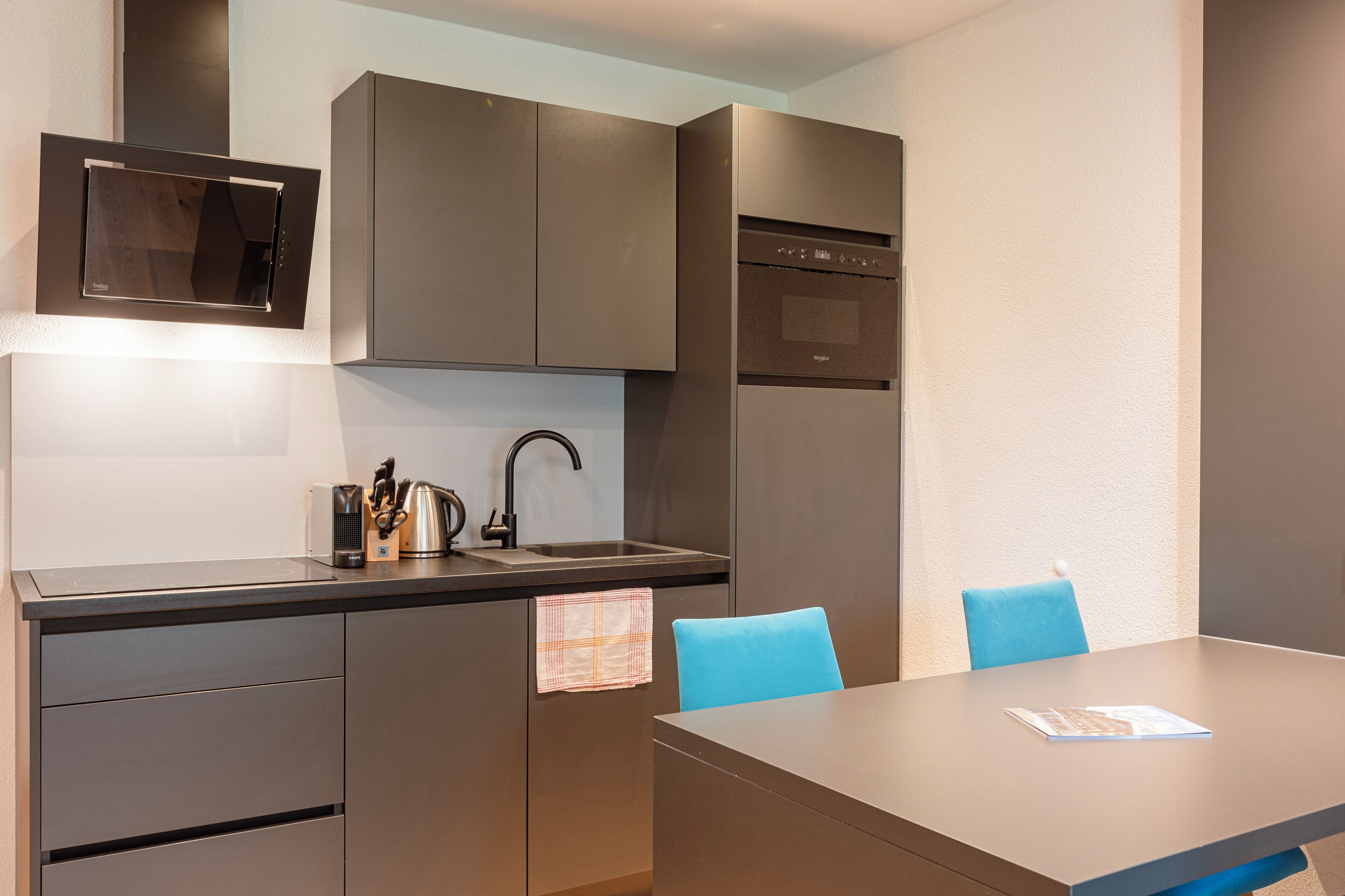Cocina compacta con electrodomésticos integrados, un lavabo y una zona de comedor con mesa y sillas.