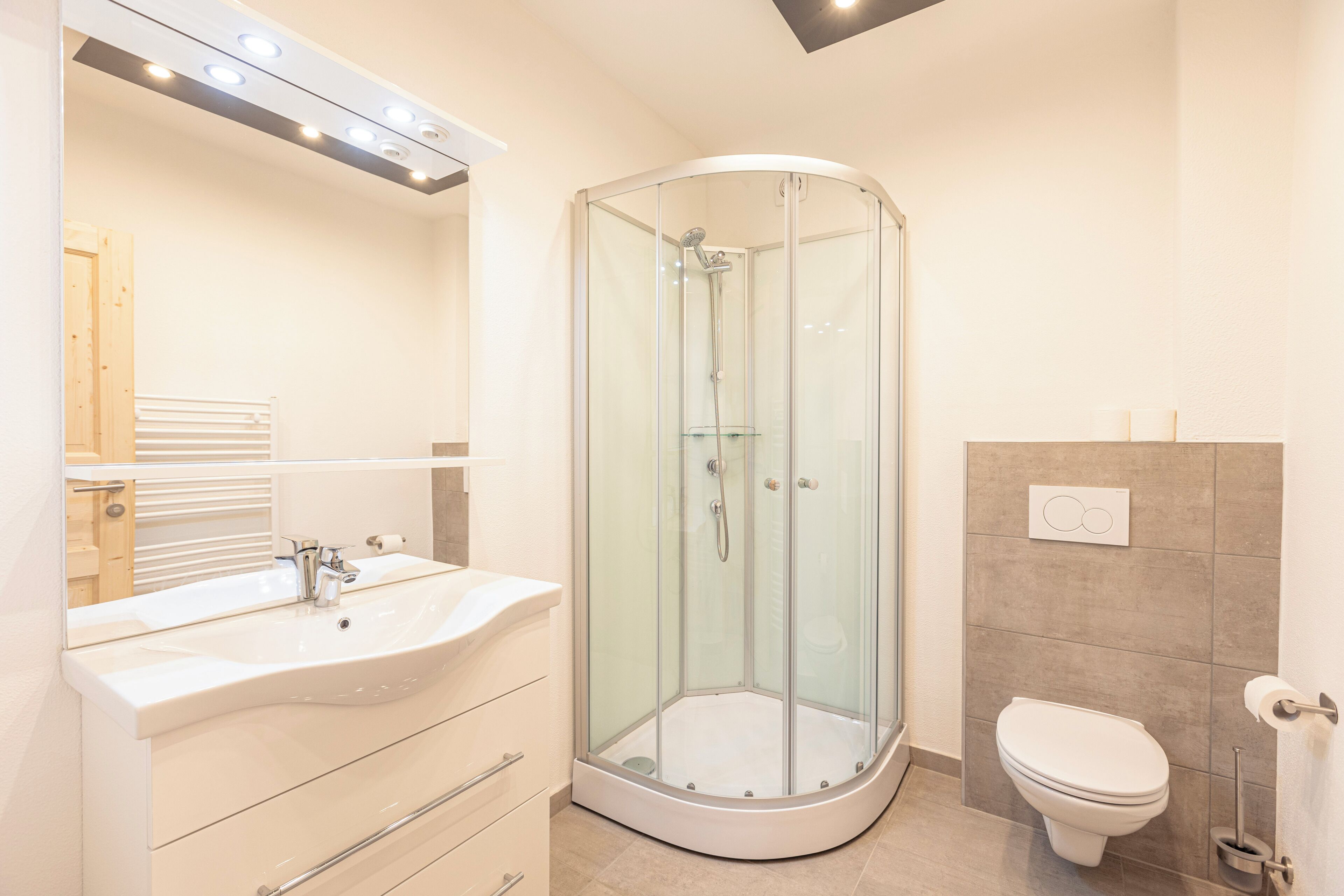 A modern bathroom with a glass-enclosed shower, a white sink with a mirror above it, and a toilet.