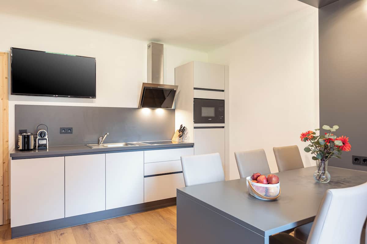 Una cocina moderna con televisor de pantalla plana, horno empotrado y comedor con mesa y sillas.