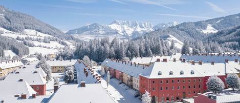 A snow-covered town with buildings, including a red building with multiple windows, and mountains in the background.
