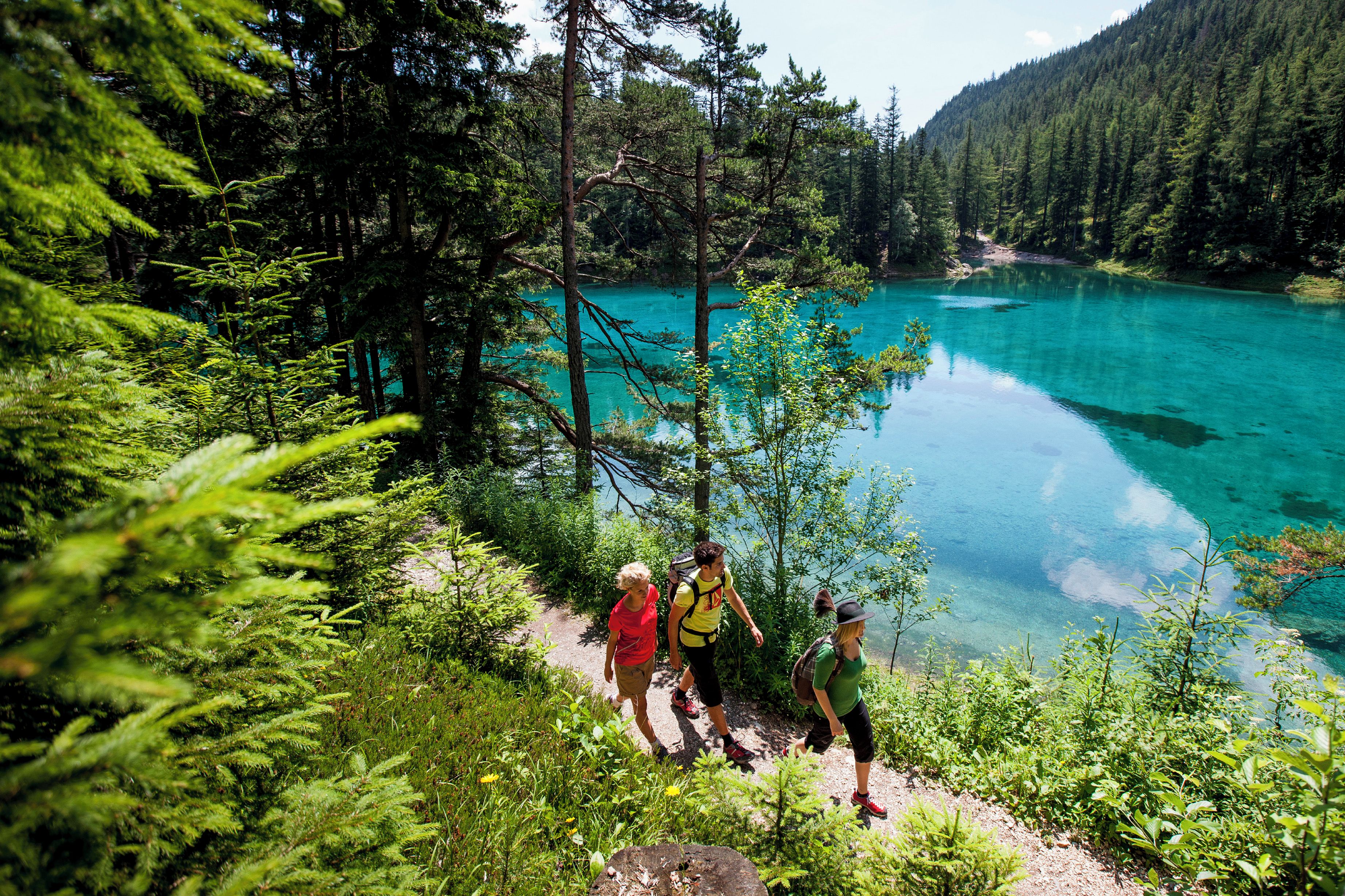 Un grupo de personas caminando cerca de un lago turquesa rodeado de un bosque denso.