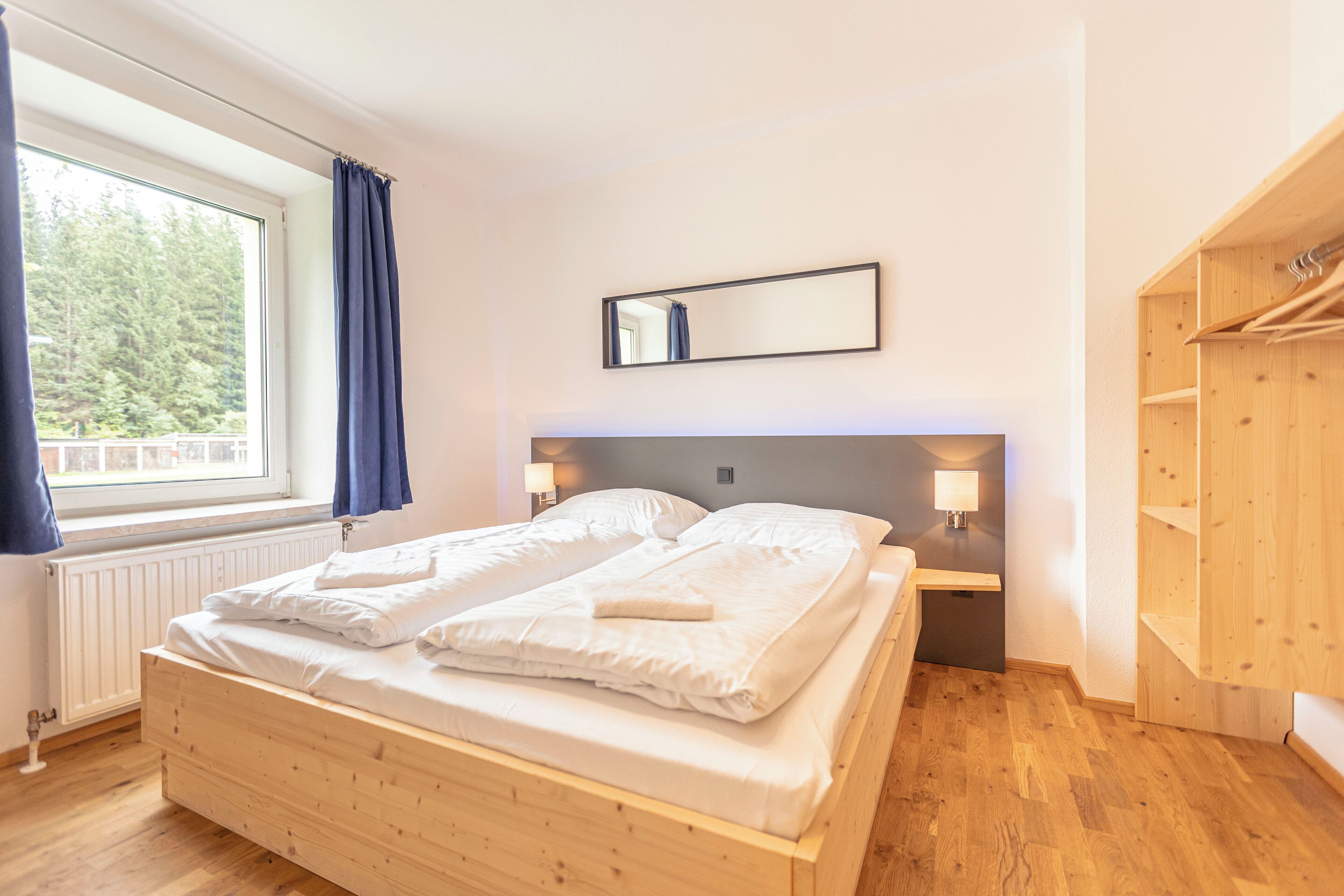 Un dormitorio con una cama de madera, una ventana con cortinas, un espejo y un armario de madera.
