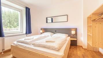 Une chambre à coucher avec un lit en bois, une fenêtre avec des rideaux, un miroir et une armoire en bois.