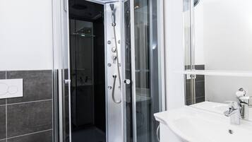 Un baño moderno con ducha de mampara de vidrio, lavabo blanco y un espejo grande.