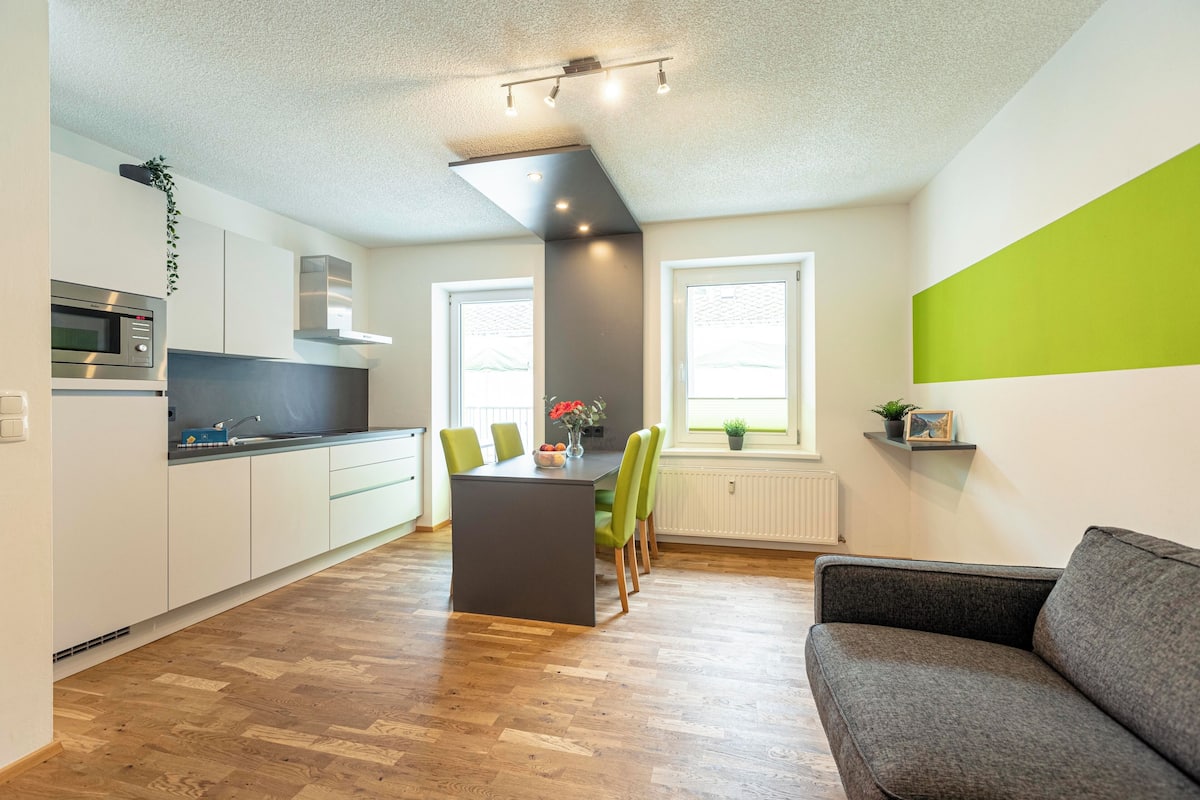 Una cocina moderna con una isla central, suelo de madera y un sofá gris en la sala de estar.