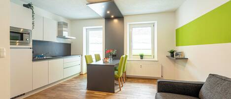 A modern kitchen with a central island, wooden flooring, and a grey sofa in a living area.
