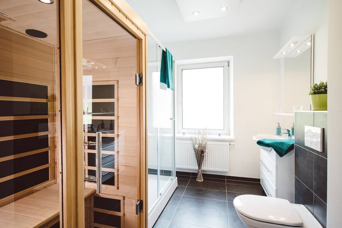 Un baño moderno con cabina de ducha de vidrio, inodoro blanco, lavamanos y una toalla verde, además de una ventana que proporciona luz natural.