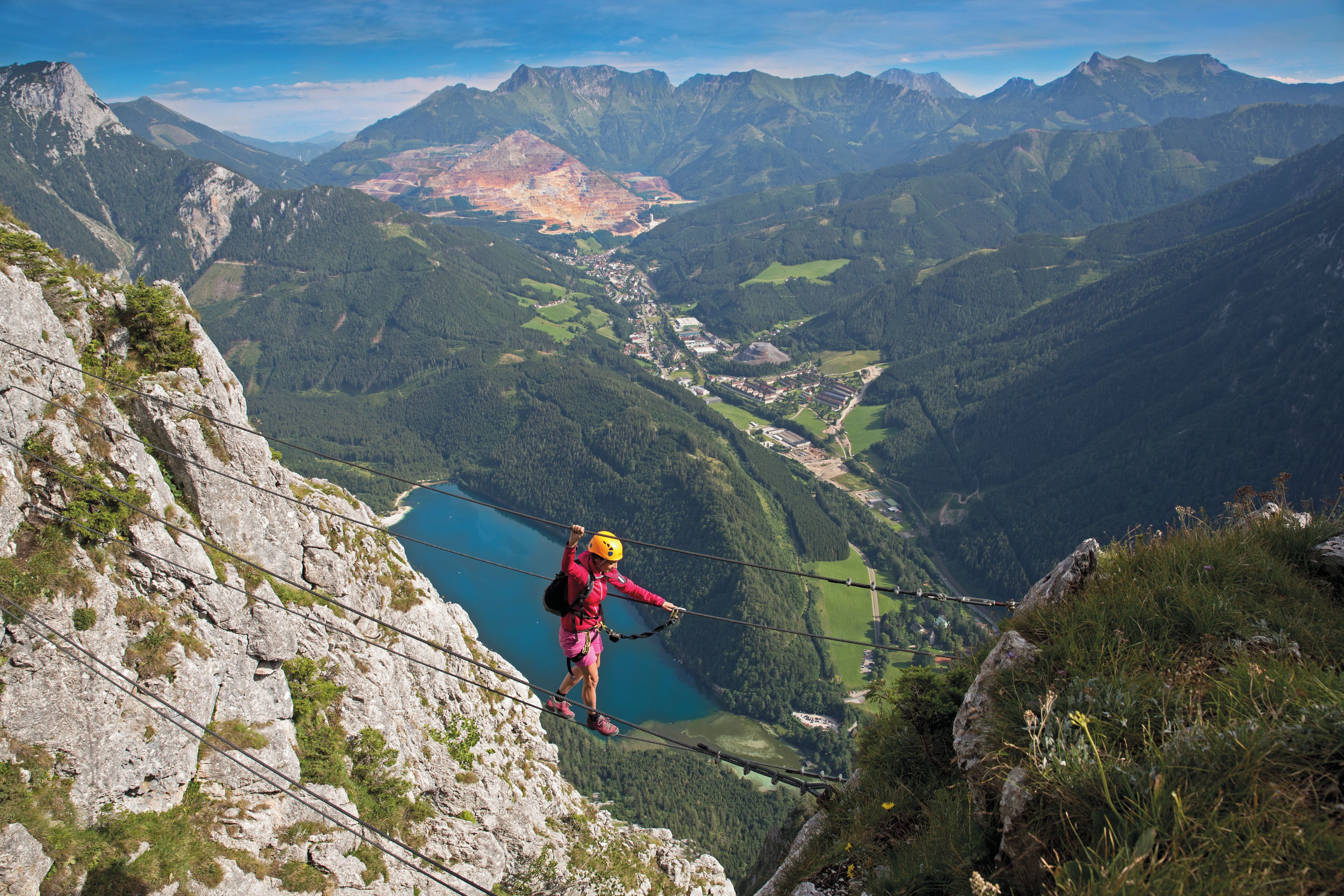 Une personne se trouve sur un pont suspendu, avec un paysage montagneux en arrière-plan.