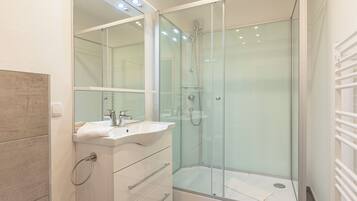 A modern bathroom with a glass-enclosed shower, a white sink with a mirror above it, and a towel rack.