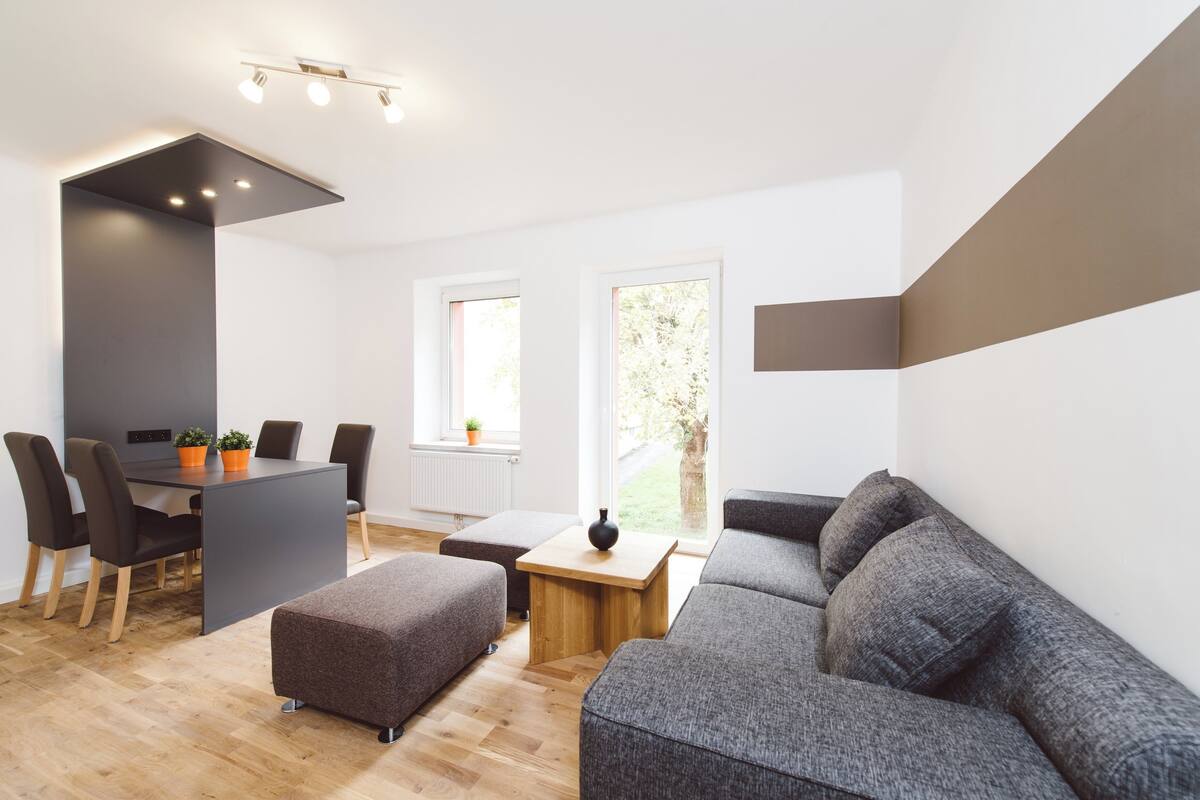 Una sala de estar moderna con un sofá gris, una mesa de comedor con sillas y una pequeña mesa de centro de madera.