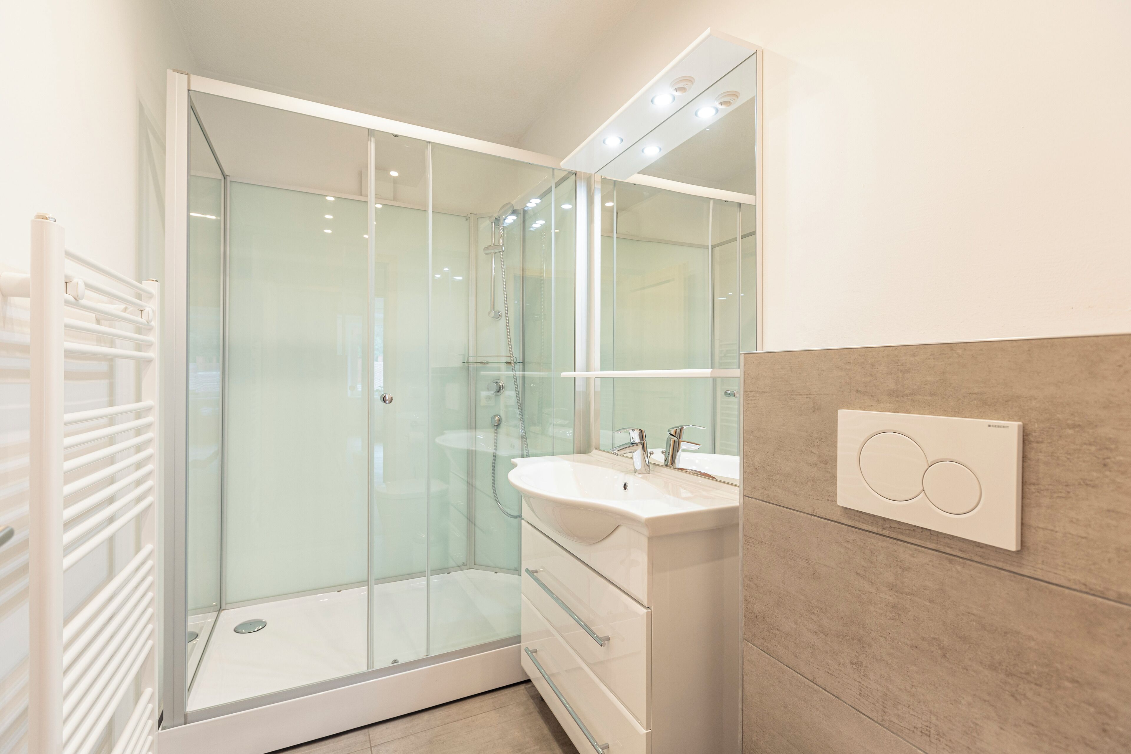 Een moderne badkamer met een douche met glazen wand, een witte wastafel en een spiegel erboven.