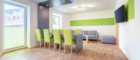 A modern dining area with a wooden floor, green chairs, a grey table, and a grey sofa.