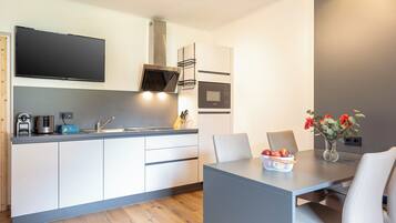 Een moderne keuken met een flatscreen televisie, magnetron en inbouwoven. Er is een eettafel met stoelen en een vaas met bloemen.