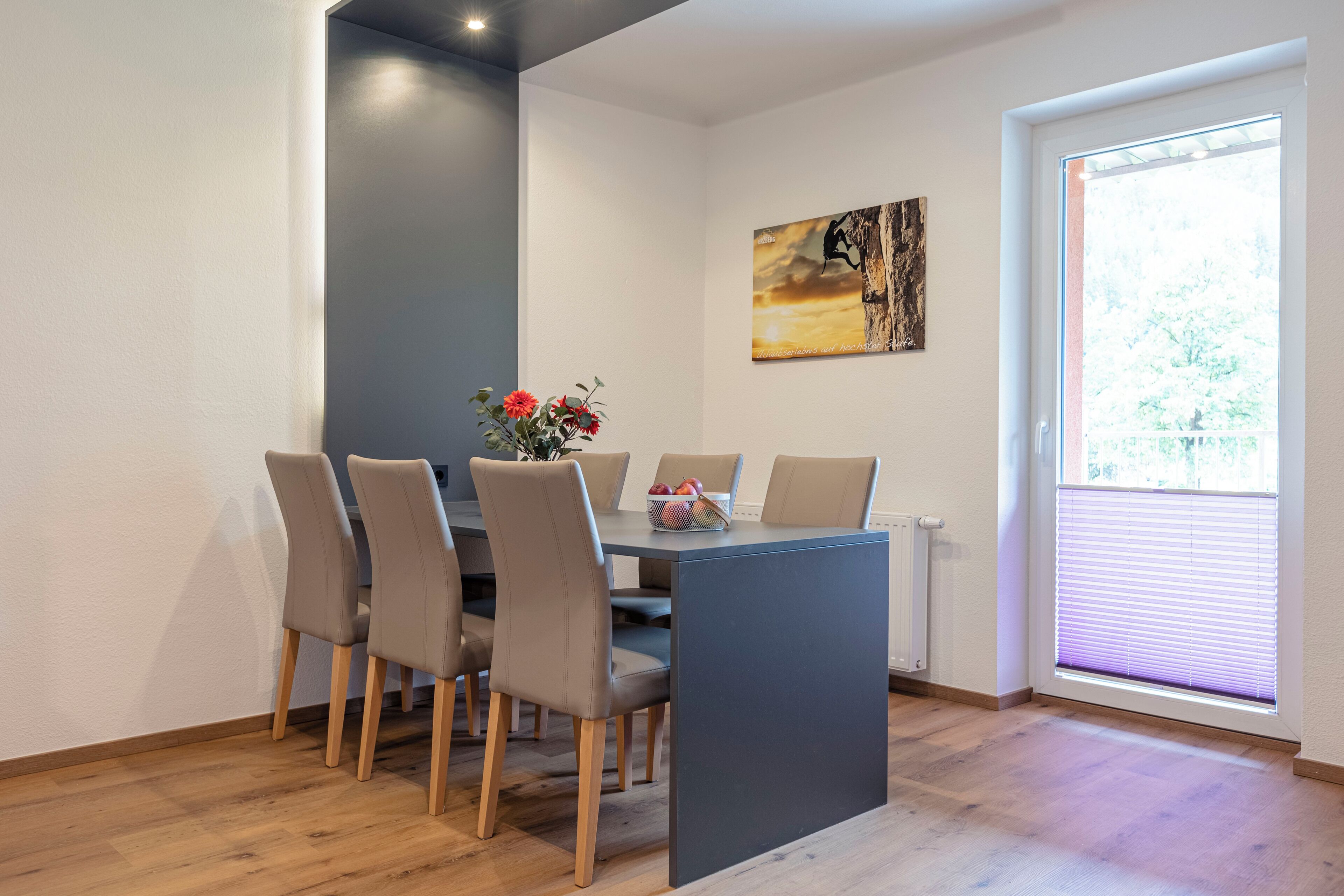 Un comedor con una mesa y sillas, un cuadro en la pared y una ventana con persianas.