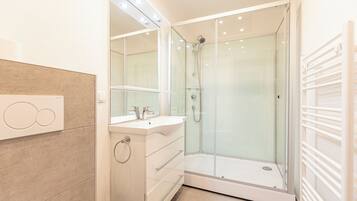 A modern bathroom with a glass-enclosed shower, a vanity with a mirror, and a towel rack.