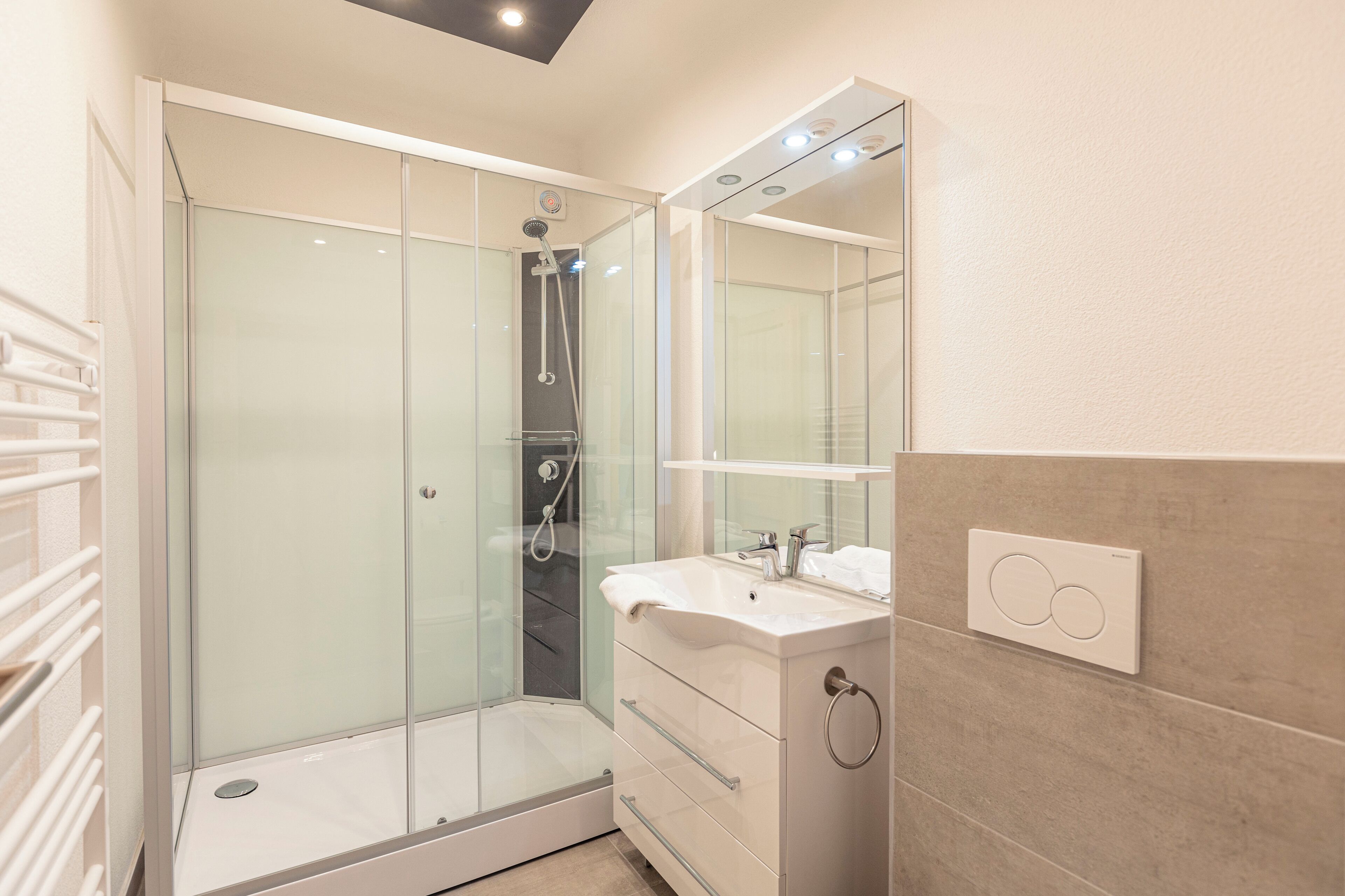 Une salle de bain moderne avec une douche à parois de verre, un lavabo blanc et un miroir au-dessus du meuble-lavabo.