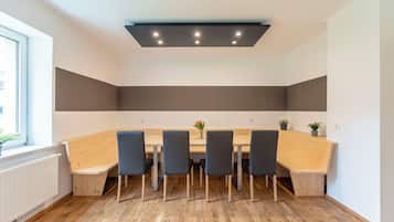 A modern dining area with a long wooden table, six chairs, and a ceiling light fixture.
