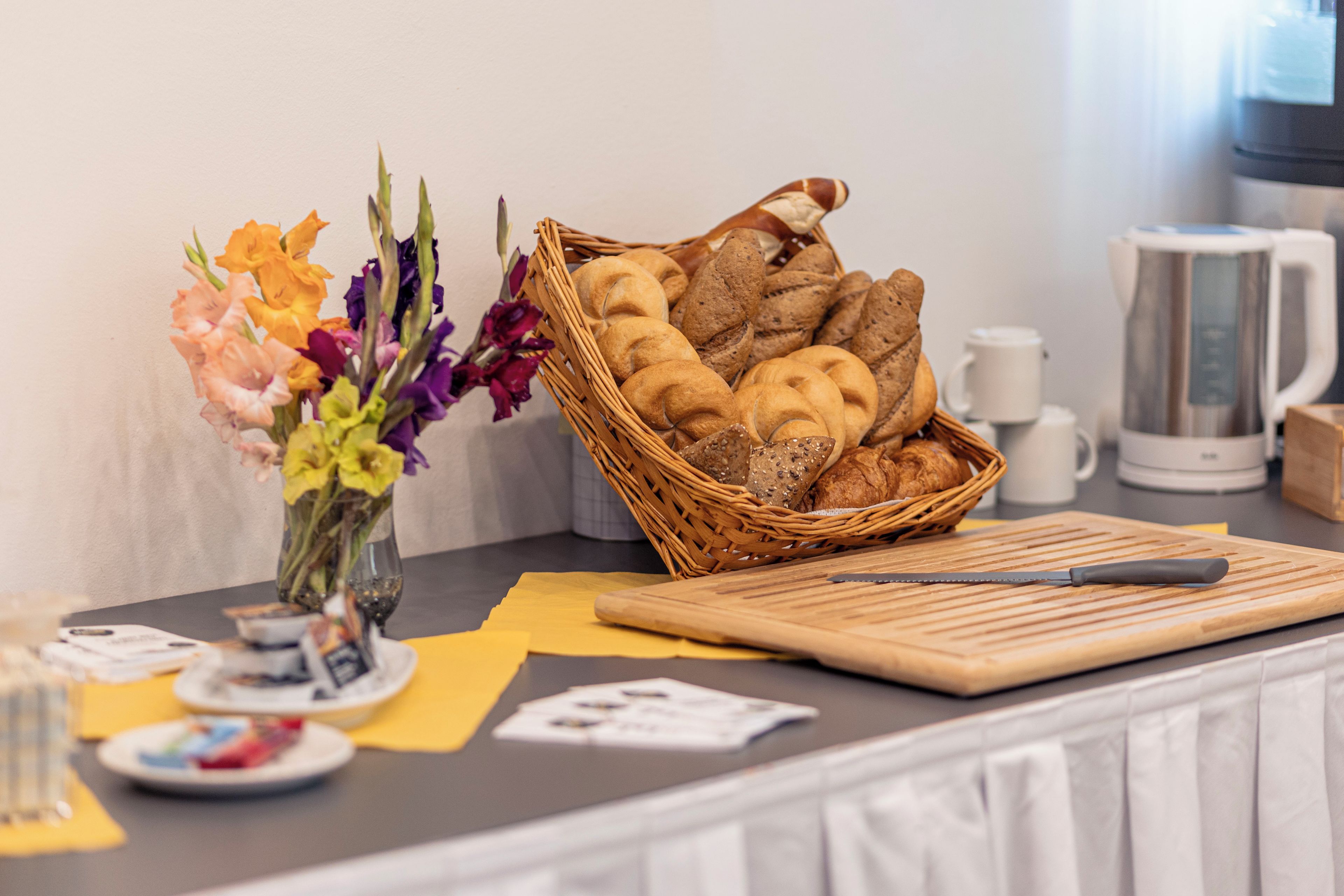 A table with a basket of bread, a vase with flowers, and a cutting board with a knife.