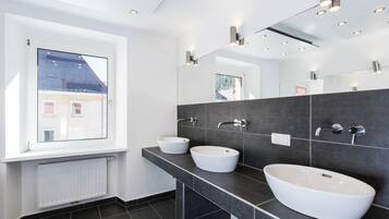 Un bagno moderno con due lavandini bianchi, pareti rivestite di piastrelle scure e un grande specchio.