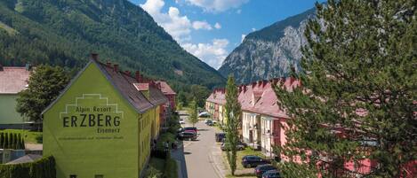 A green building with 'Alpin Resort ERZBERG Eisenerz' signage, surrounded by residential houses and a mountainous backdrop.