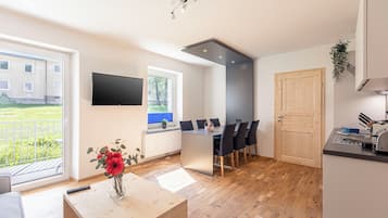 A modern kitchen with a dining area, a TV mounted on the wall, and a view of the outside.