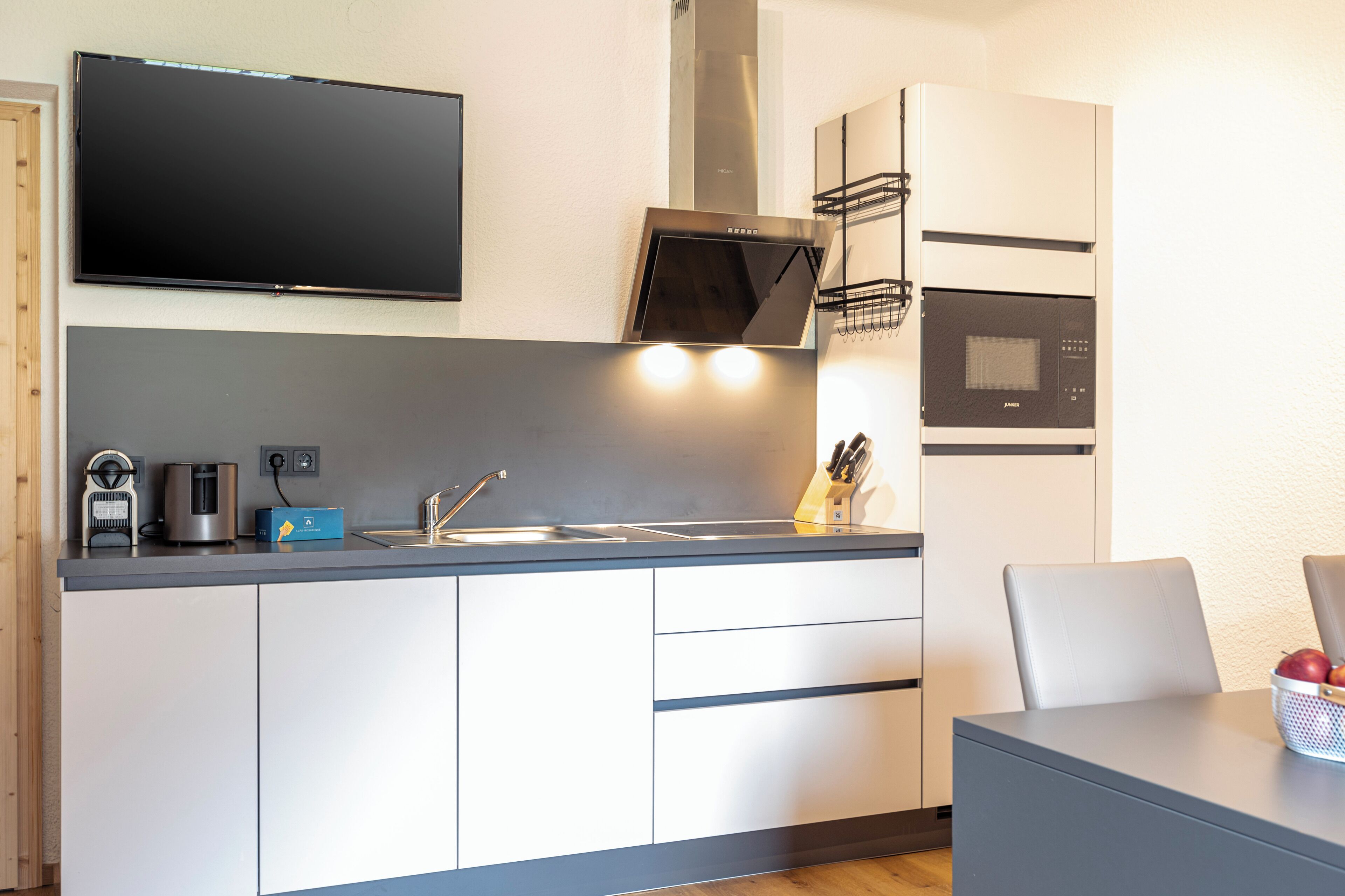 A modern kitchen with a flat-screen TV, built-in oven, microwave, and a sink.