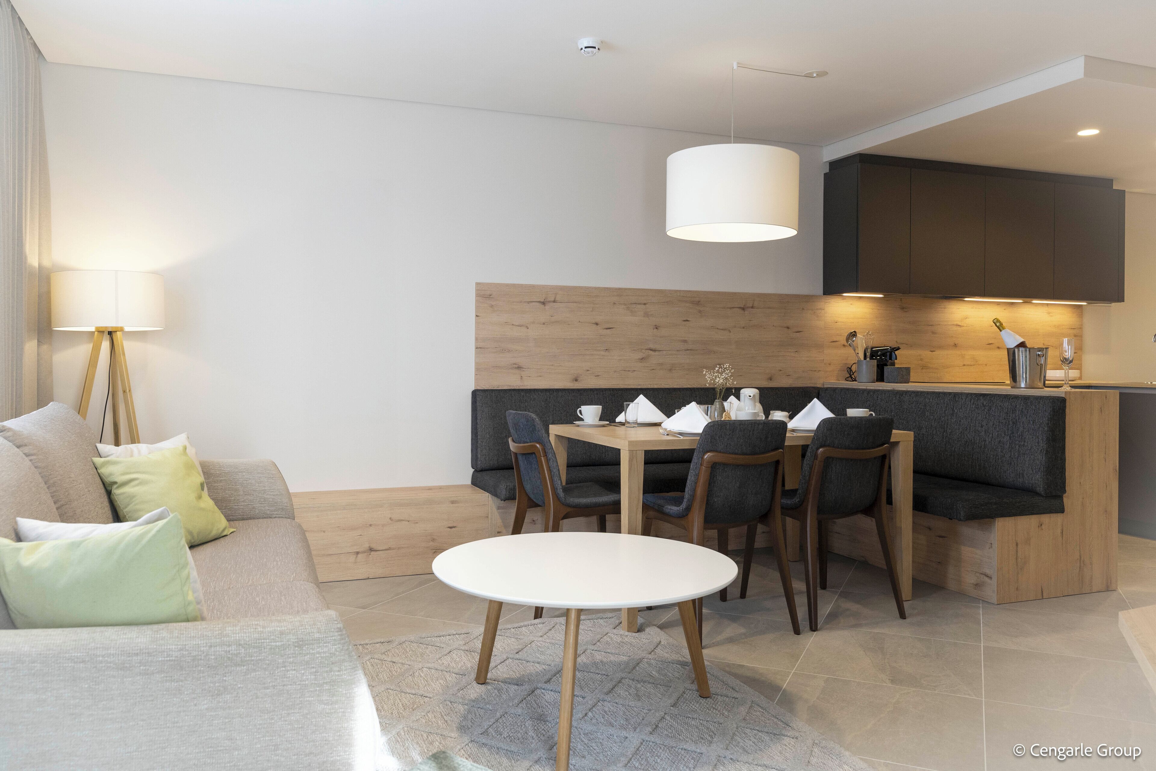 Ein modernes Wohnzimmer mit einer Couch, einem Esstisch mit Stühlen, einer Lampe und einer Küchenzeile mit Schränken und einer Arbeitsplatte.